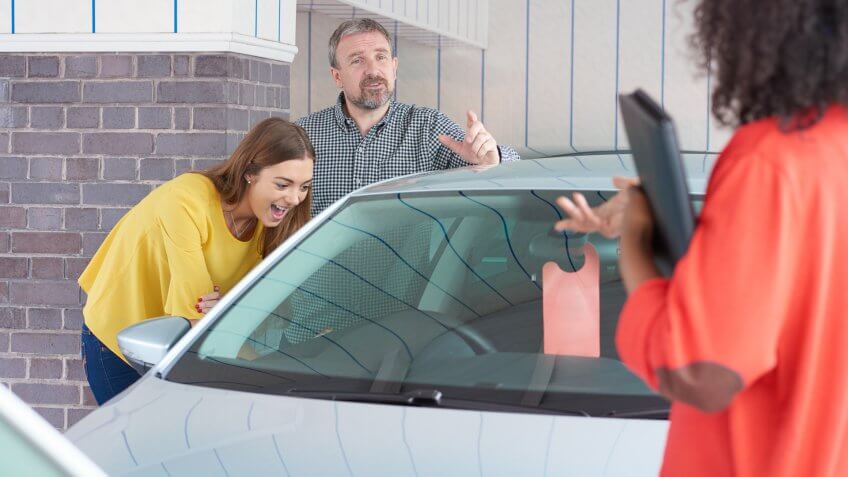 A mature man and his young daughter are looking at cars in a car showrooms .
