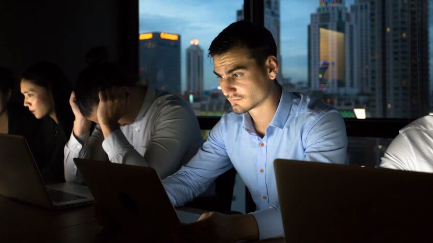 business team working late at night with lights off and computers laptop screen light on.