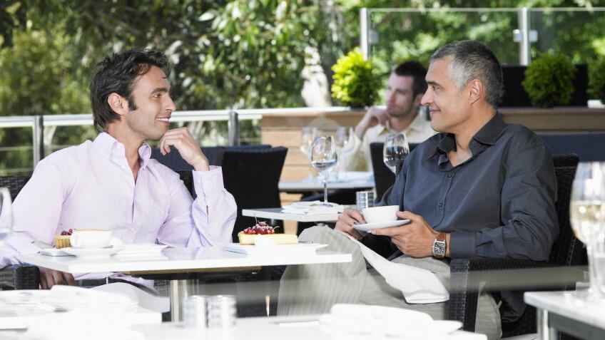 Happy businessmen conversing at outdoor cafe.