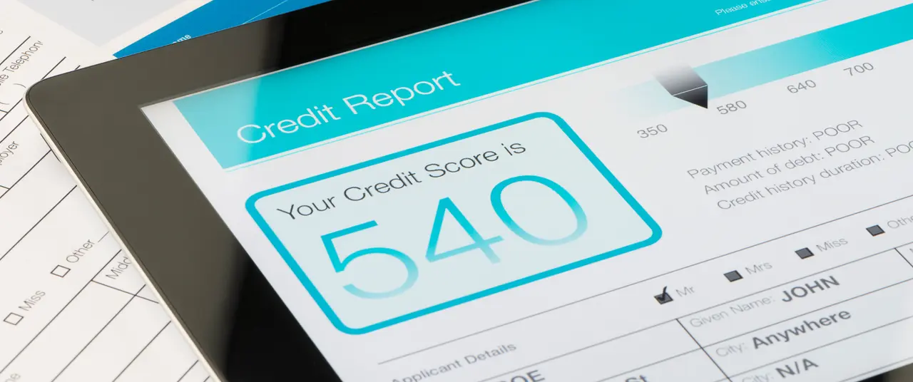 Credit report on a digital tablet with paperwork.