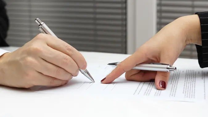 A close-up image of two hands with pens in them going over paperwork.