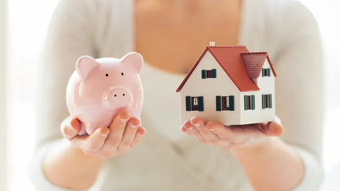 woman holding piggy bank and toy house