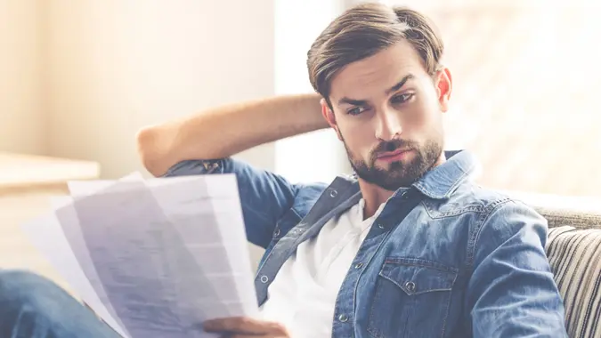 Handsome businessman in casual wear is studying documents while sitting on couch at home.