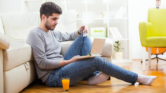 Handsome man holding credit card and using laptop for online shopping - indoors.