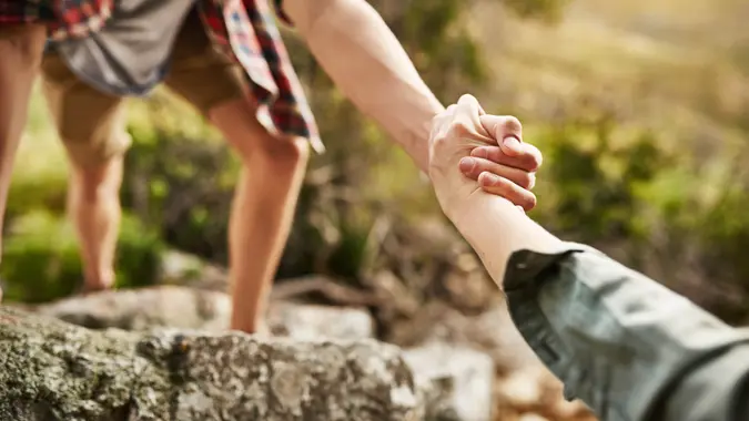hikers helping each other climb up a rock in nature