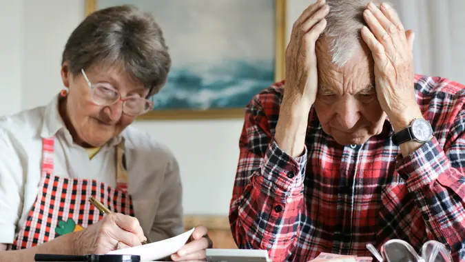 Desperate senior couple counting money from retirement, little savings, filling checks and control finance sitting at the table in the living room.