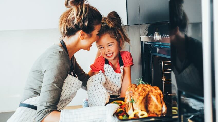 Little girl watching her mother taking the turkey out of the oven.