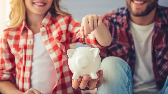 Young woman is putting a coin into a piggy bank that a man is holding.