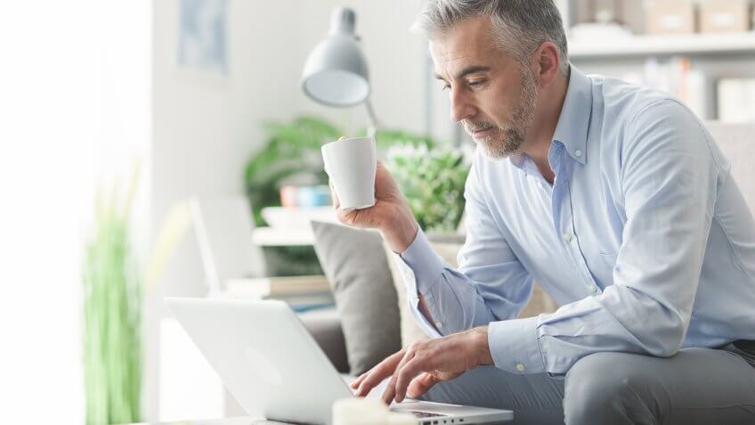 senior older man drinking coffee looking at his laptop