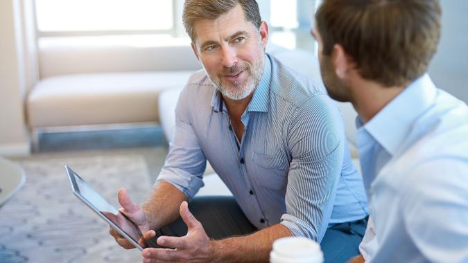 man holding ipad tablet speaking to another man