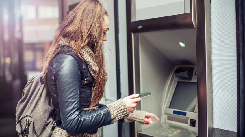 Young woman withdrawing money from credit card at ATM.