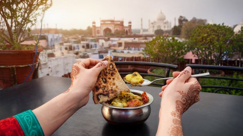 How Much to Tip When Traveling to These 25 Countries, India, Uttar Pradesh, Woman eating traditional Indian food in rooftop restaurant with