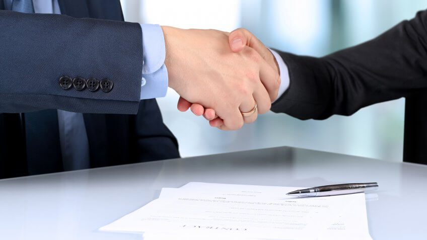 Close up of man and woman shaking hands over documents