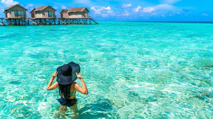How Much to Tip When Traveling to These 25 Countries, Portrait of happy young woman at beautiful water villa at Maldiv