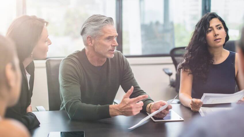 Older man speaking to colleagues at a meeting