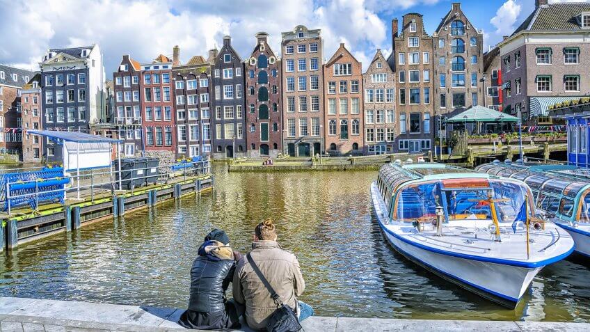 How Much to Tip When Traveling to These 25 Countries, Netherlands., Young love couple sitting on the waterfront against the canal in