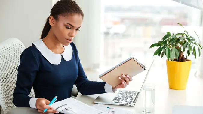 young woman sitting at desk with laptop and paperwork