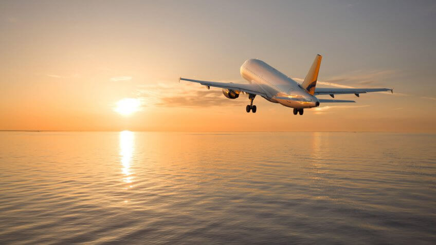 airplane flying over the ocean at sunset