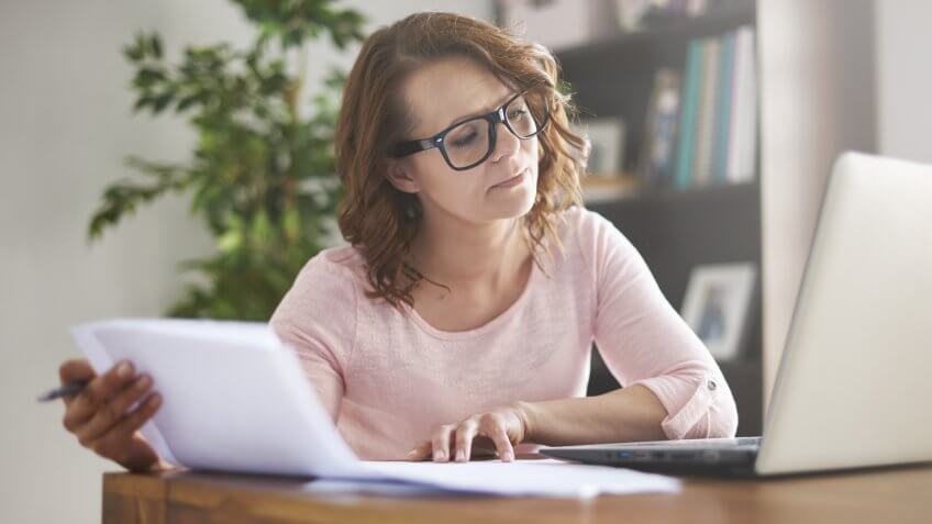 woman on laptop at desk holding documents