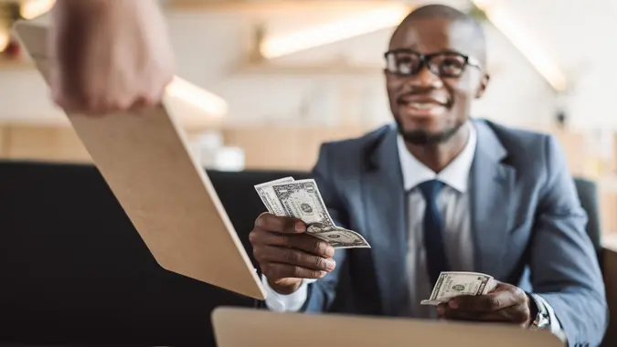 A smiling man or businessman handing cash over to cover a check at a restaurant or cage.