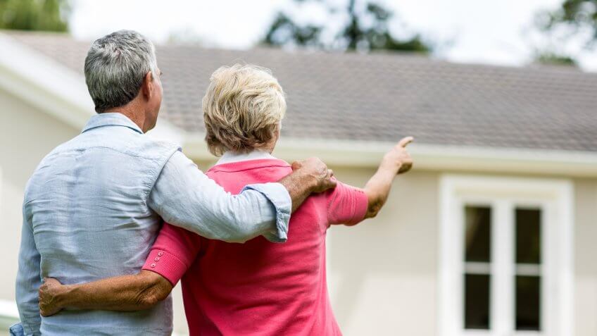 Rear view of senior couple looking at house while standing in yard.