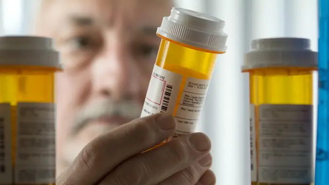 A senior man examining prescription drugs in a cabinet or home and weighing prices, finances, side effects, more.