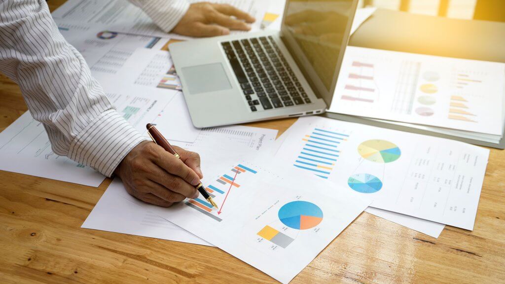 Gates says it is important to set a goal and measure your progress. person working on laptop and examining several papers filled with graphs and charts