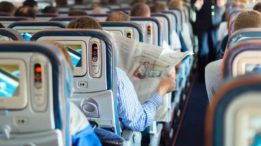 Person in airplane aisle seat reading a newspaper Person in airplane aisle seat reading a newspaper
