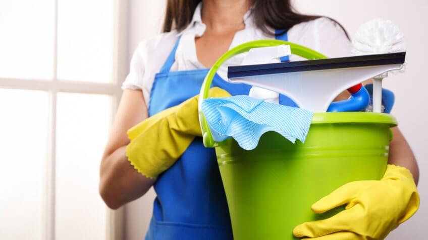 Woman in blue apron holding a green plastic bucket with cleaning tools