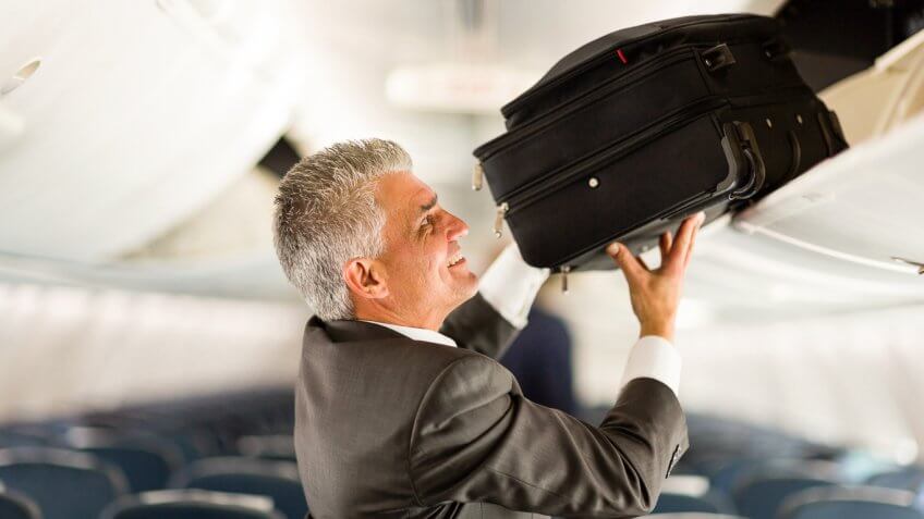 Man placing luggage in overhead compartment on airplane Man placing luggage in overhead compartment on airplane