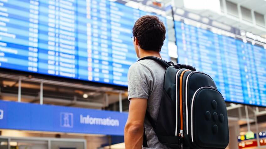 Man with backpack looking at electronic flight arrival/departure board Man with backpack looking at electronic flight arrival/departure board