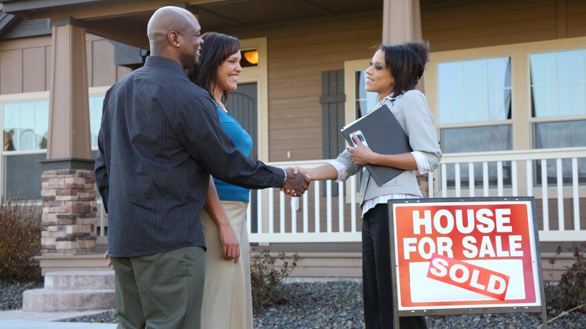 Couple shakes hands with realator in fron of new home.
