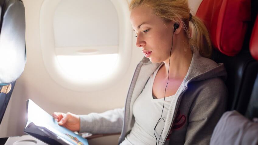 Woman wearing earbuds and reading a book or magazine Woman wearing earbuds and reading a book or magazine