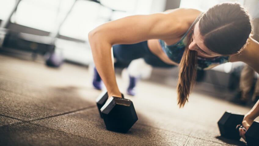 Woman doing push-up exercise with dumbbell.