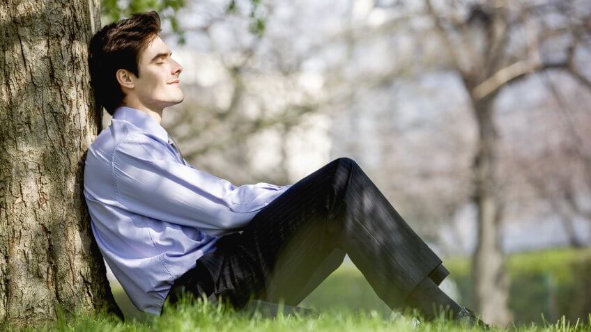 content man sitting against a tree in the park