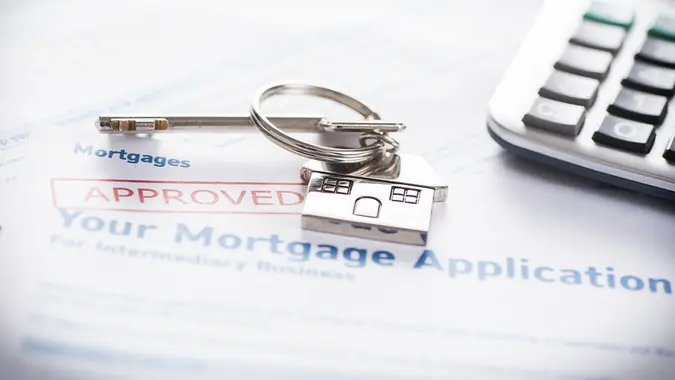 A calculator and a set of keys with a house keychain on top of an approved mortgage application.
