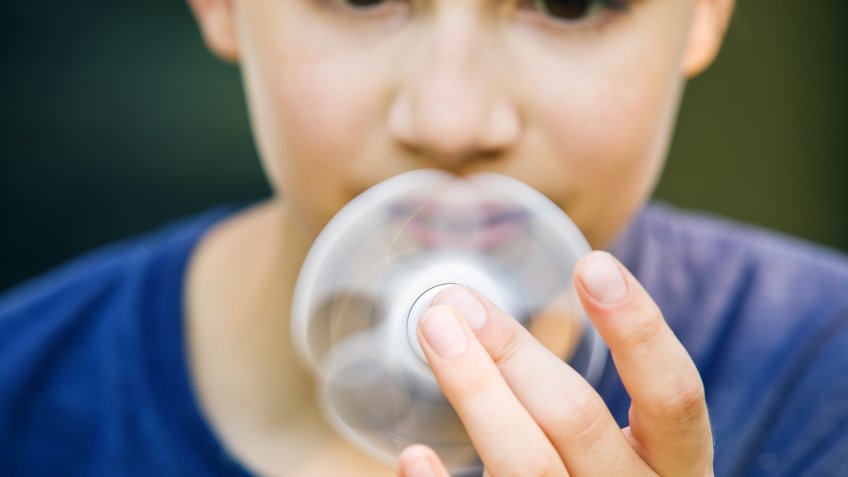 A 13 year old boy holding a spinner close to his face.