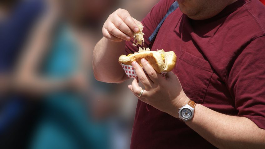 obese person putting sauerkraut on a hot dog