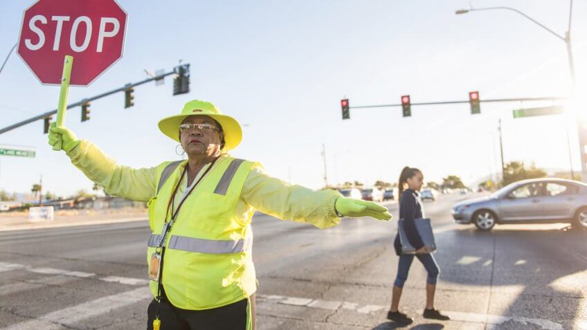 Crossing guard Patricia Bass assists a child in crossing Lake Mead Boulevard at Tonopah Drive before classes at West Preparatory Academy in Las Vegas, Thursday, Oct.