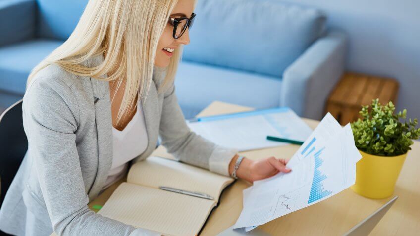 Happy young woman working with financial data from home office.
