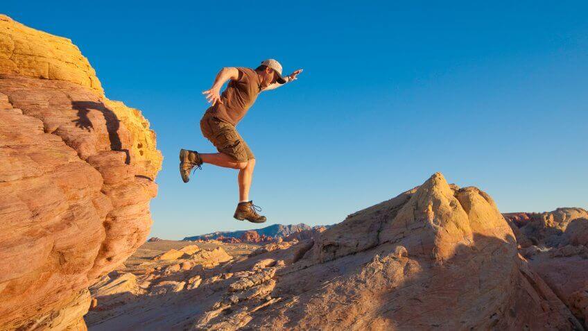 A man leaps down from a mountain.