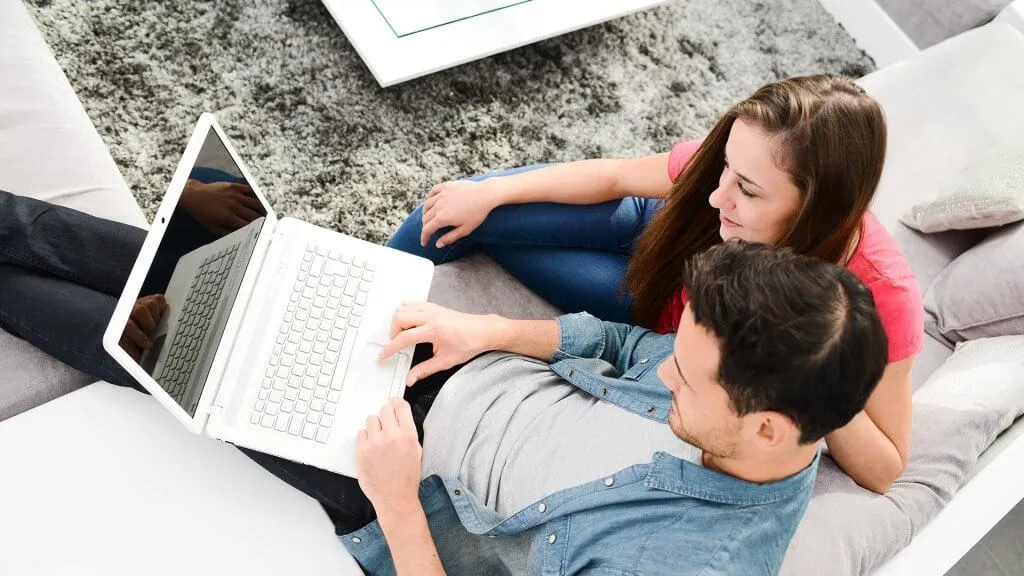 couple sitting on couch looking at laptop