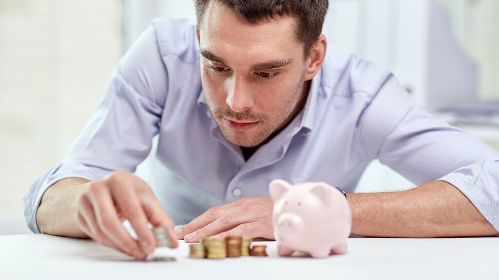 Reevaluate Other Savings Goals man carefully placing coins in stacks next to piggy bank