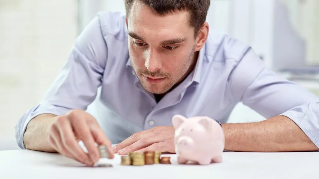 man carefully placing coins in stacks next to piggy bank