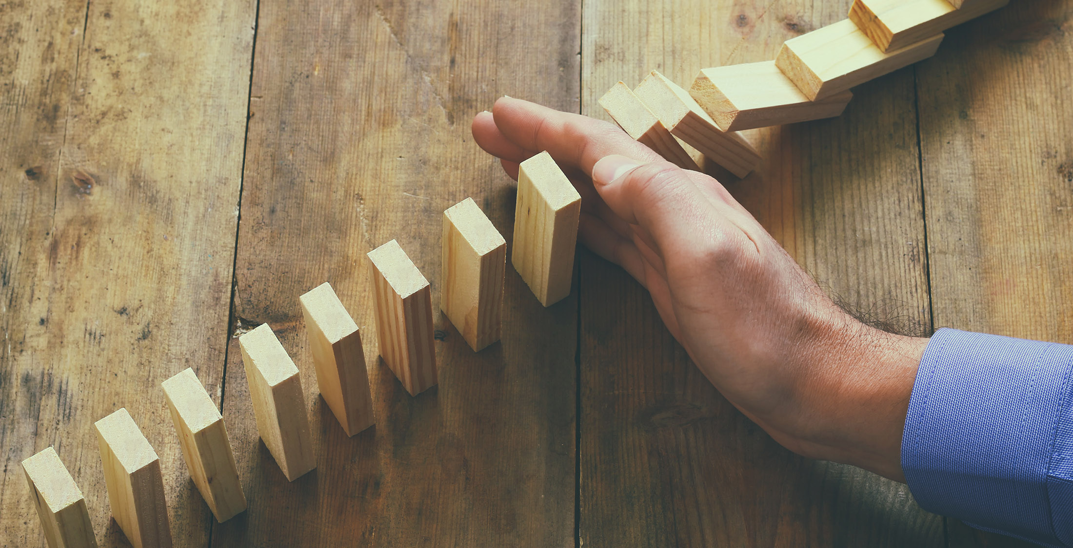 Look at some small investment opportunities hand blocking row of wooden blocks from falling