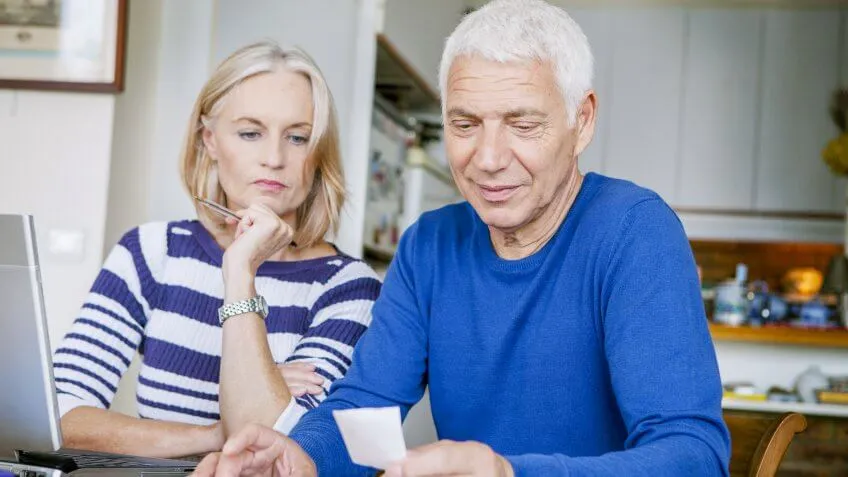 older couple studying piece of paper near laptop