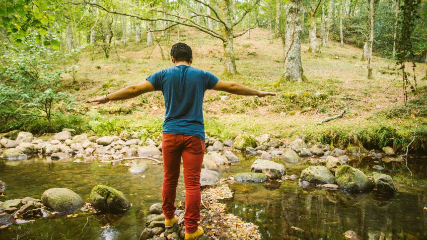 young man walking across a creek