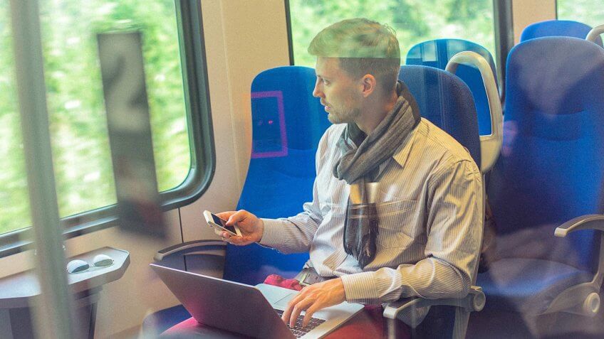 young man using his computer and smartphone on a train
