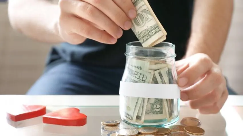 close up of man placing dollar bills in a jar