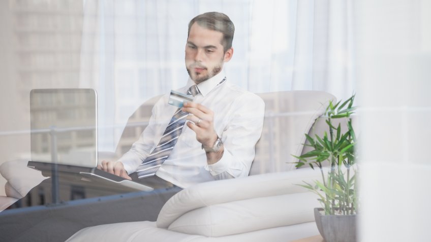 Businessman shopping online on his couch seen through glass at home in the living room.